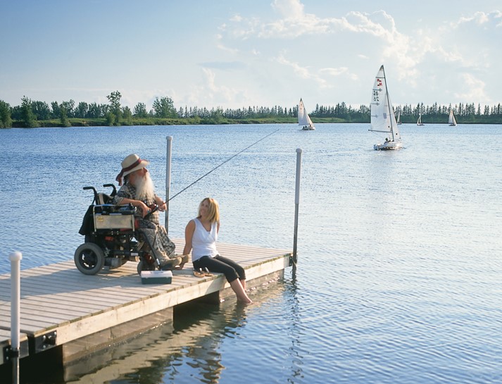 Man in wheelchair on a dock, fishing while beside a woman.