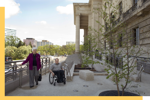 Une personne en fauteuil roulant et une personne qui marche sur la rampe de l’édifice de l’Assemblée législative du Manitoba. 
