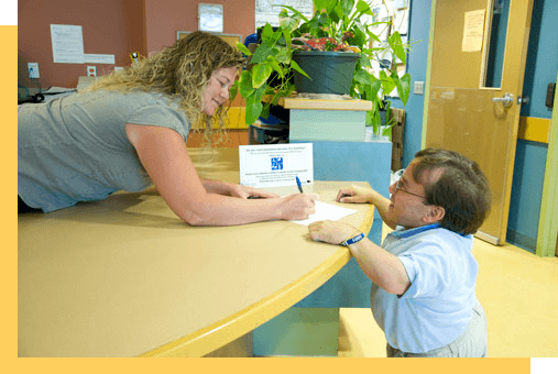 A person greeting another person at a desk.